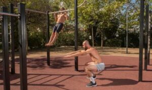 Två män tränar kroppsvikt utomhus med pull-ups och knäböj